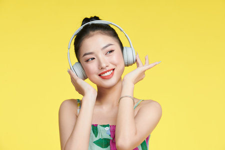 Cheerful young woman listen to music putting her hands on headphones isolated on yellow backgroundの写真素材