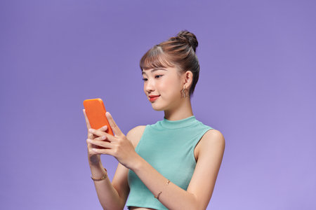 Pretty millennial girl isolated on purple background text messaging on cell phoneの写真素材