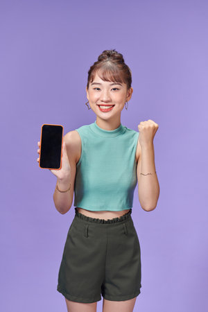 Young excited woman hold mobile cell phone with blank screen workspace area do winner gesture clenched fistの写真素材