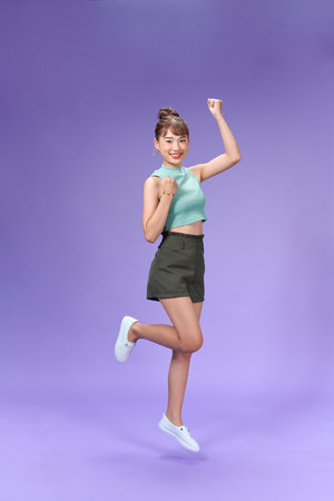 Full length portrait of a joyful young woman jumping and celebrating over purple backgroundの写真素材