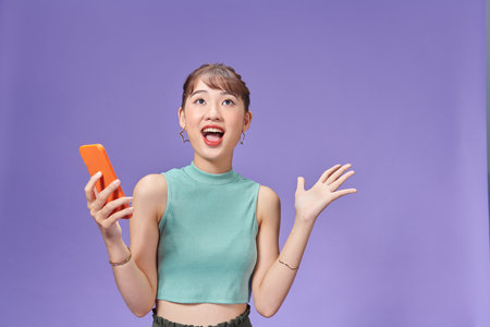 Happy asian woman feeling happiness and standing hold smartphone other hand open on purple backgroundの写真素材
