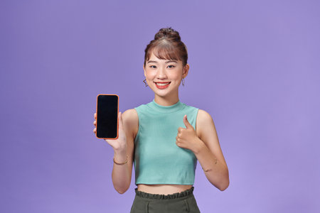 Satisfied happy asian girl show thumbs-up as demonstrate mobile phone screen applicationの写真素材
