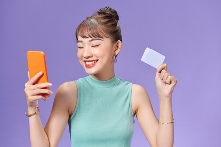 smiling girl holding a credit card and mobile phone online shoppingの写真素材