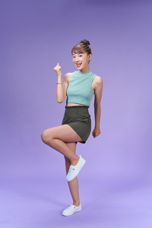 Full length of attractive young woman looking at camera and smiling while standing against purple backgroundの写真素材