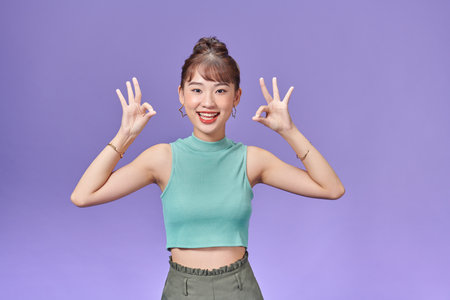 Cute woman with okay hand gesture isolated on purple background.の写真素材
