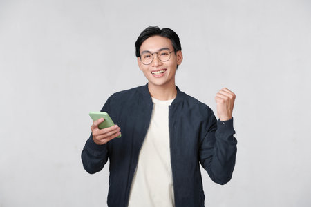 Happy man holding smartphone and celebrating his success over white backgroundの写真素材