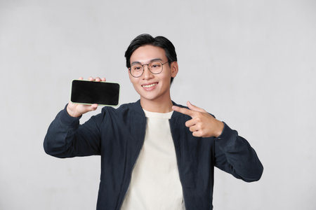 Young man holding smartphone in his hand and pointing his finger on blank screenの写真素材