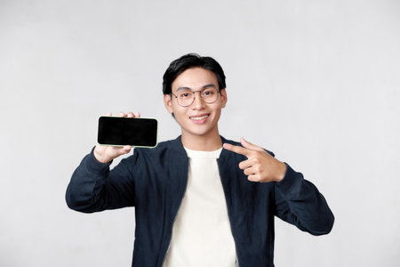 Young man pointing with his index finger at the mobile phone with blank screenの写真素材