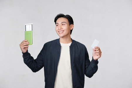 A satisfied young man holding passport with tickets and showing plastic credit card isolated over white backgroundの写真素材
