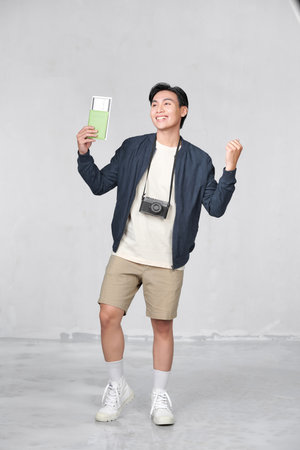 Portrait of happy young guy holding passport and boarding pass against white backgroundの写真素材