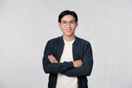 young man keeping arms crossed and smiling while standing against white backgroundの写真素材