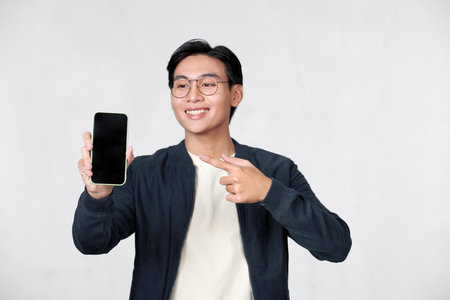Young man holding smartphone in his hand and pointing his finger on blank screenの写真素材