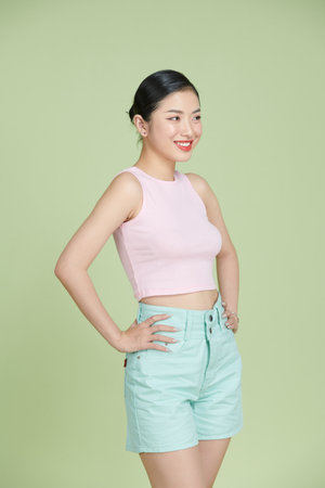 Cute slim feminine young woman in top tank and summer shorts with hands on hips smiling at cameraの写真素材