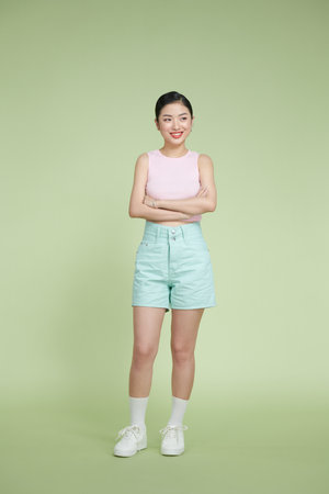 Full length of smiling young asian girl in casual clothes  holding hands crossed on pastel green backgroundの写真素材