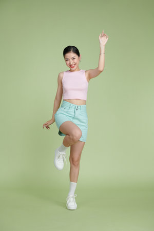 Full body of happy girl dancing your hands up on green pastel backgroundの写真素材