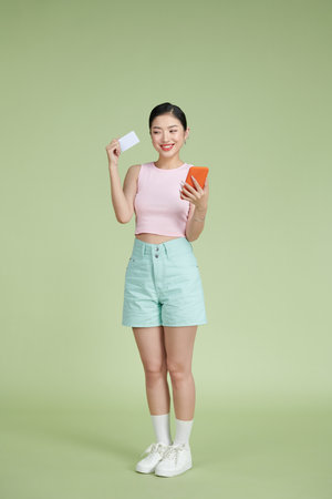 Portrait of a smiling woman holding credit card and mobile phone over greenの写真素材