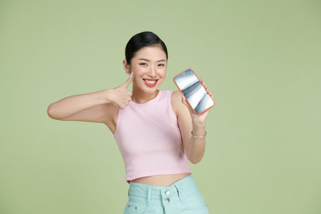Portrait of smiling asian woman holding smartphone with black blank device screen in hand, showing thumb up gestureの写真素材