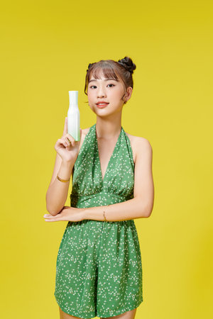 young asian girl in the studio with cosmetics bottles on a yellow backgroundの写真素材