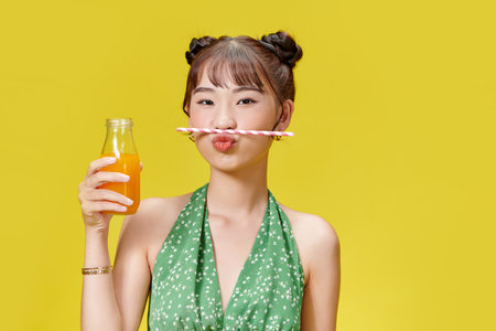 Young asian woman holding fresh orange juice from bottle, spending time with pleasure indoorsの写真素材
