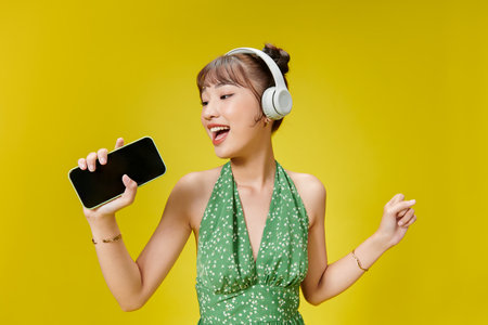 Photo of adorable trendy woman in summer wear listening to music via wireless headphones and holding cell phoneの写真素材