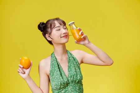 Close up, smiling woman with orange juice over yellow backgroundの写真素材