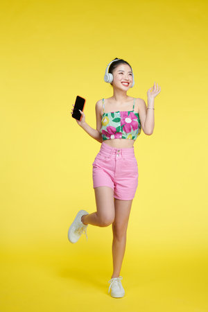 Happy cheerful Asian woman wearing wireless headphones listening to music from smartphoneの写真素材