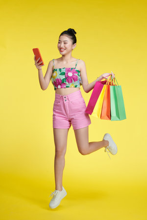 Full length of happy young attractive shopaholic woman raising shopping bags and holding mobile phoneの写真素材