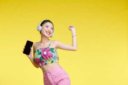Cute beautiful woman listening to music using wireless headphones isolated over yellow background.の写真素材