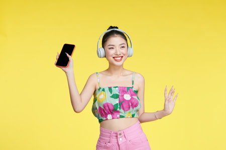 Cute beautiful woman listening to music using wireless headphones isolated over yellow background.の写真素材