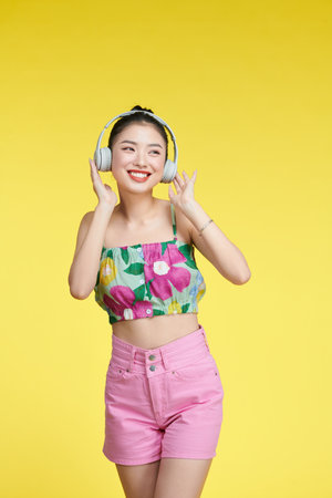 Cheerful young woman listen to music putting her hands on headphones isolated on yellow backgroundの写真素材