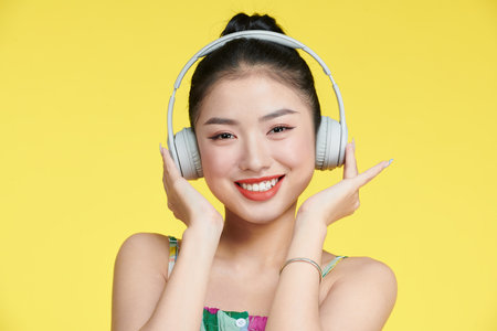 young woman singing while listening music with headphones isolated over yellow backgroundの写真素材