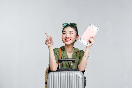 Enthusiastic asian girl shows passport tickets, smiling pleased, standing with suitcase, gray backgroundの写真素材