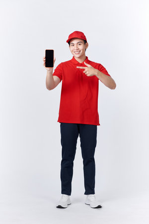 Asian delivery man wearing cap holding smartphone over white background very happy pointing with hand and finger to the sideの写真素材