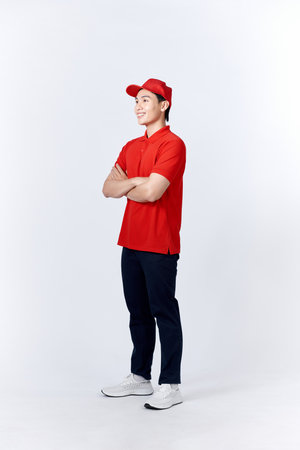 Young asian man in uniform red and cap standing arms crossed with confident isolated on white backgroundの写真素材