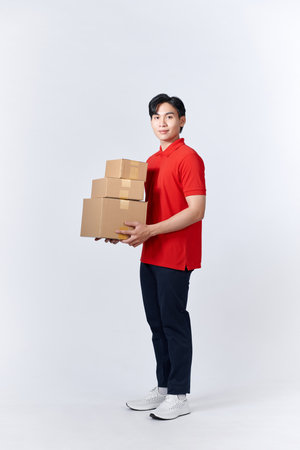 young man in red shirt carrying three carton boxes on a white wallの写真素材