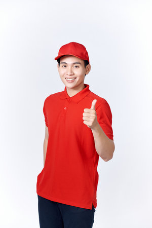Professional delivery guy employee man in red cap T-shirt uniform workwear work as dealer courier showing thumb up like gesture isolatedの写真素材