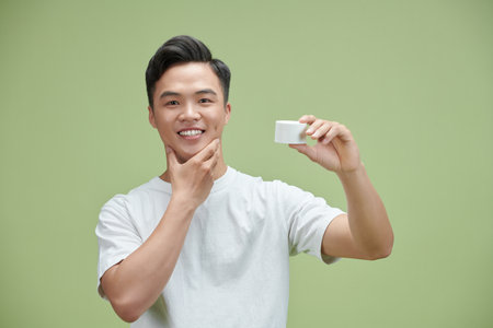 Portrait of young Asian man with cosmetics bottleの写真素材