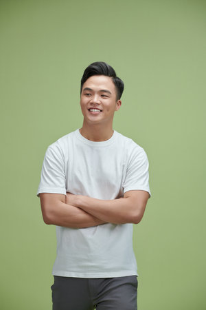 Smiling young Asian man with arms crossed in green studio isolated backgroundの写真素材