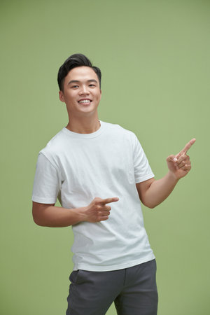 Handsome healthy young Asian man smiling with his finger pointing isolated on light greenの写真素材