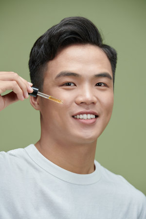 Selective focus of handsome asian man using pipette for applying serum on green backgroundの写真素材