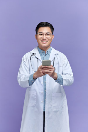 Happy doctor man texting on a smart phone isolated on a purple backgroundの写真素材