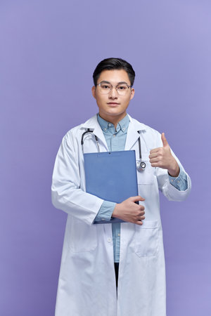 Young asian man wearing doctor uniform doing thumb up sign with fingers, excellent symbolの写真素材