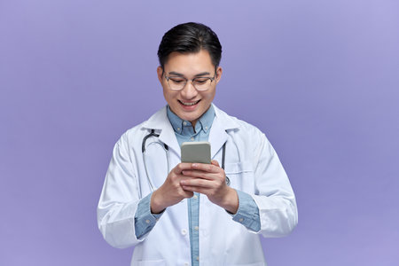 Happy doctor man texting on a smart phone isolated on a purple backgroundの写真素材