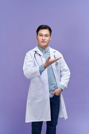 Young handsome doctor man wearing stethoscope, smiling cheerful presenting and pointing with palm of handの写真素材