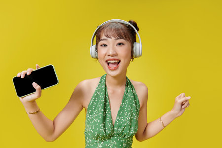 Happy young woman in headphones listening to music on vivid yellow backgroundの写真素材