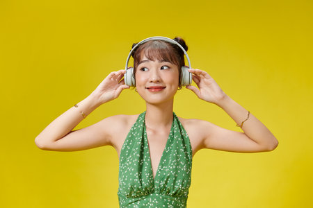 Young pretty Asian woman wearing headphones listening to music on yellow backgroundの写真素材