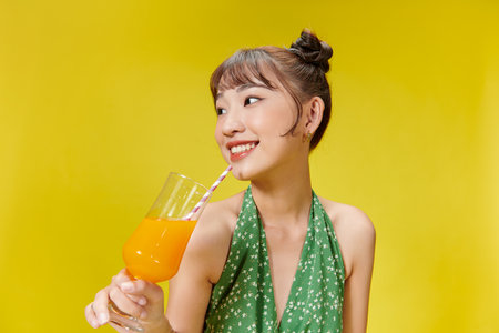 Beautiful woman drinks cocktail on yellow backgroundの写真素材