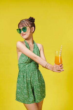 Happy Asian woman holding a glass of fruit juice drink isolated on yellow backgroundの写真素材