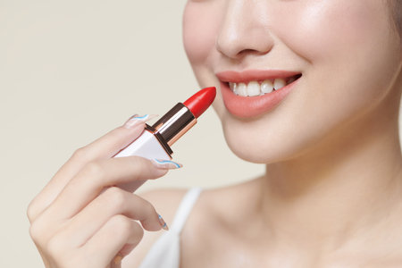 woman isolated on beige background holding red lipstickの写真素材