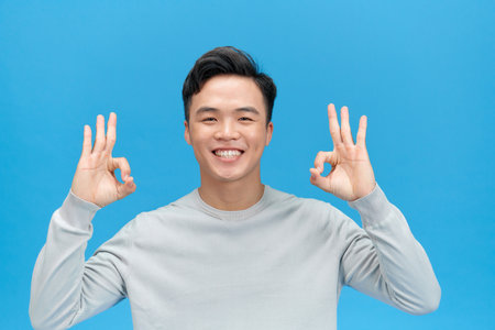 Portrait of handsome man showing ok sign and smiling isolated over blue backgroundの写真素材